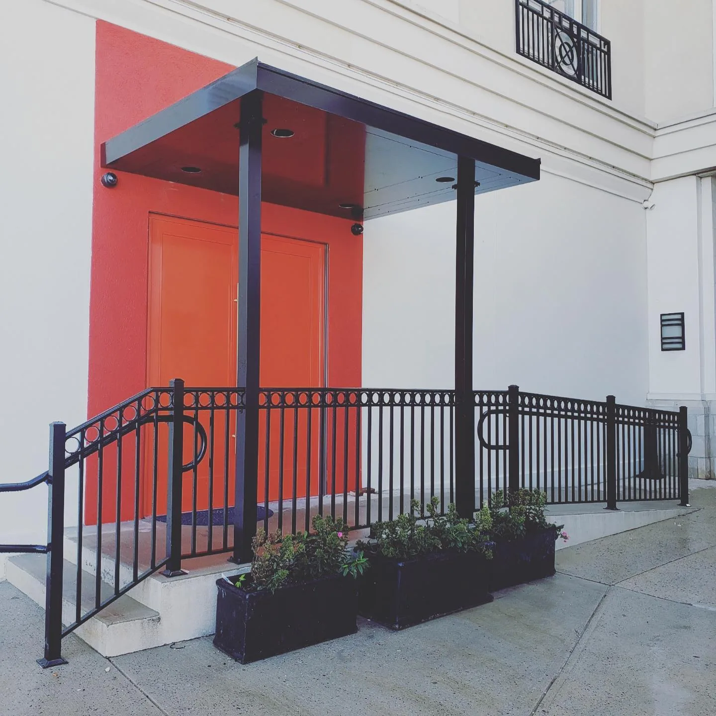 Black aluminum entrance canopy above a doorway on a light-colored building facade.