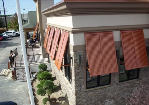 Orange-brown louvered exterior shutters above windows on a stone and stucco building.