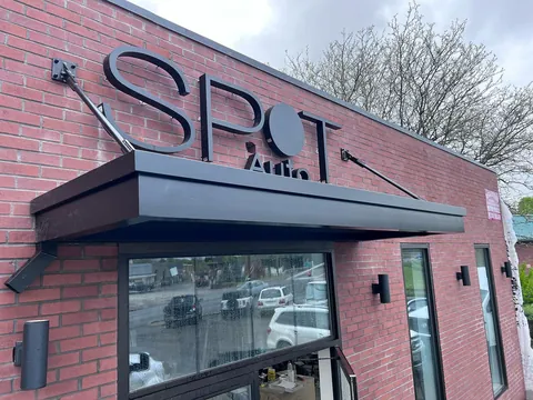 Black aluminum canopy with overhead support rods above a glass entry on a brick wall.