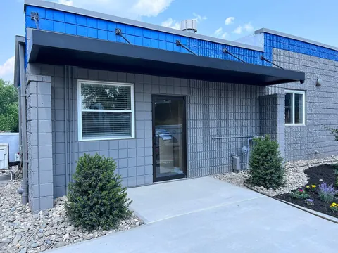 Black aluminum canopy with tie-rod supports on a gray and blue masonry building.