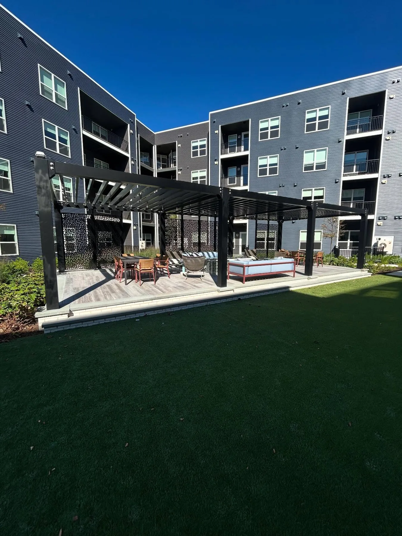 Black aluminum pergolas with decorative screens in a multifamily courtyard amenity area.