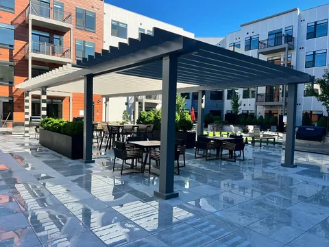 Dark gray pergola with a slatted roof over a furnished courtyard patio.