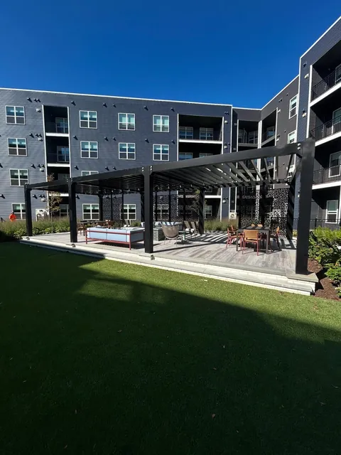 Black aluminum pergola with decorative screens and outdoor furniture on a deck.