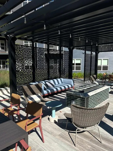 Black aluminum pergola with decorative screens and lounge furniture around a fire pit.