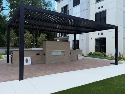 Black louvered pergola above a brick outdoor fireplace and kitchen area.