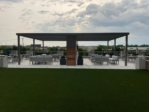 Large dark aluminum pergola over a tiled patio with outdoor seating and turf.