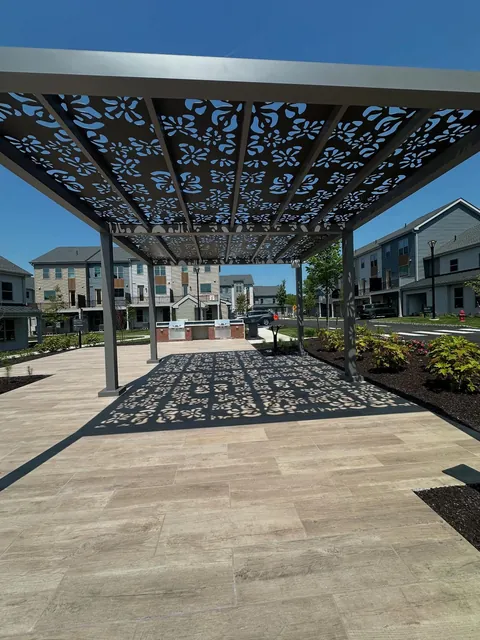 Gray freestanding pergola with floral-pattern roof panels over a tiled patio.