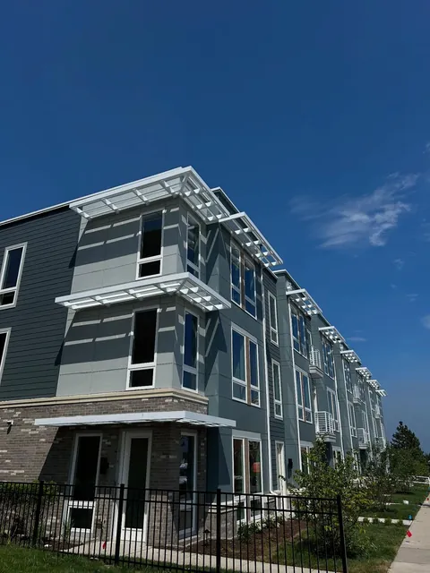 White trellis-style shade structures mounted above windows and doors on a multistory building.